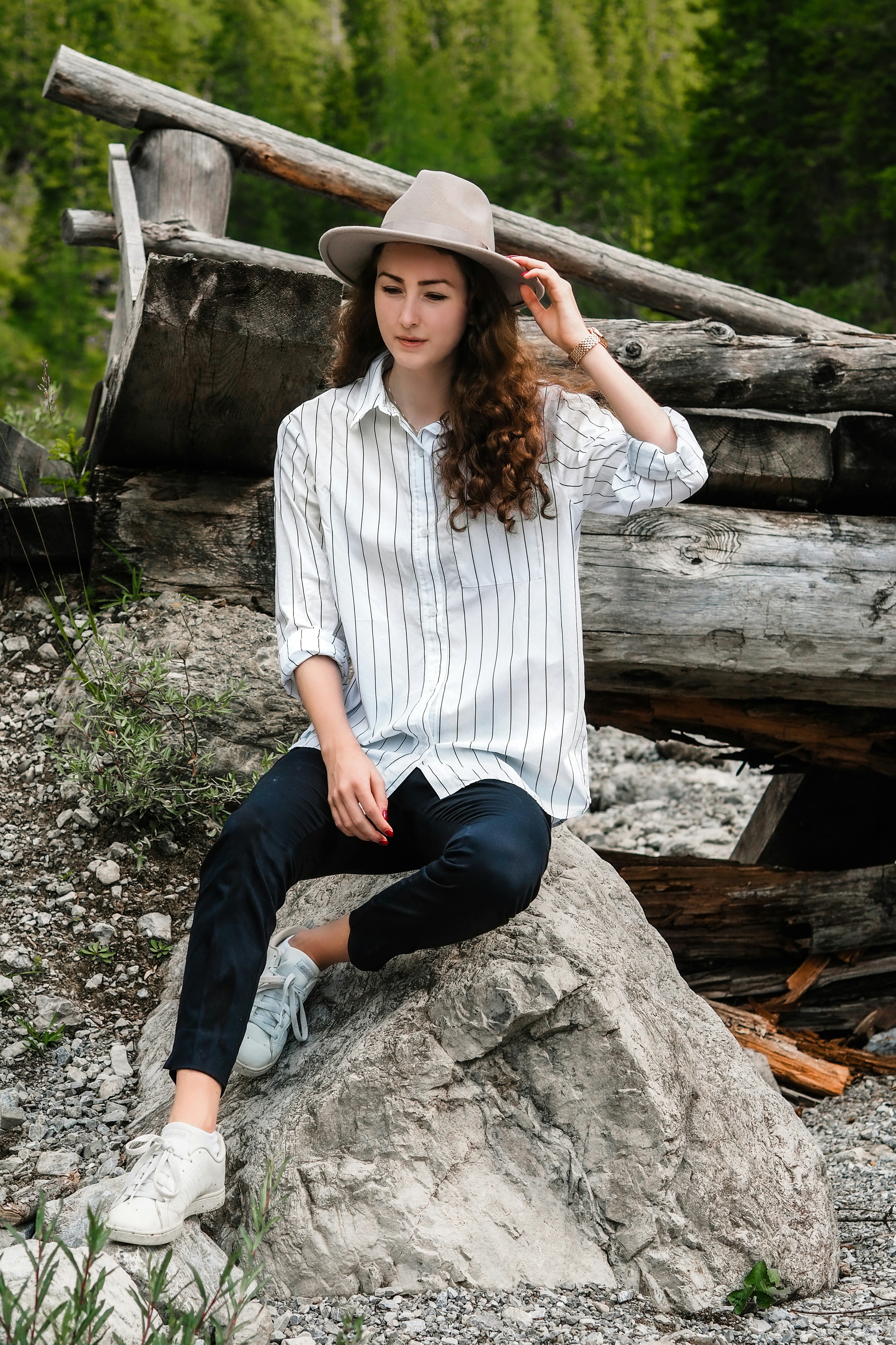 woman in white and black stripe dress shirt and black pants sitting on brown wooden log